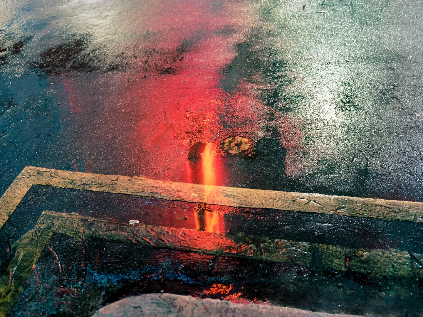 Red and yellow light reflects on a wet street with a yellow painted curb.