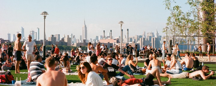 A large group of people relax on a grassy area with a city skyline in the background.