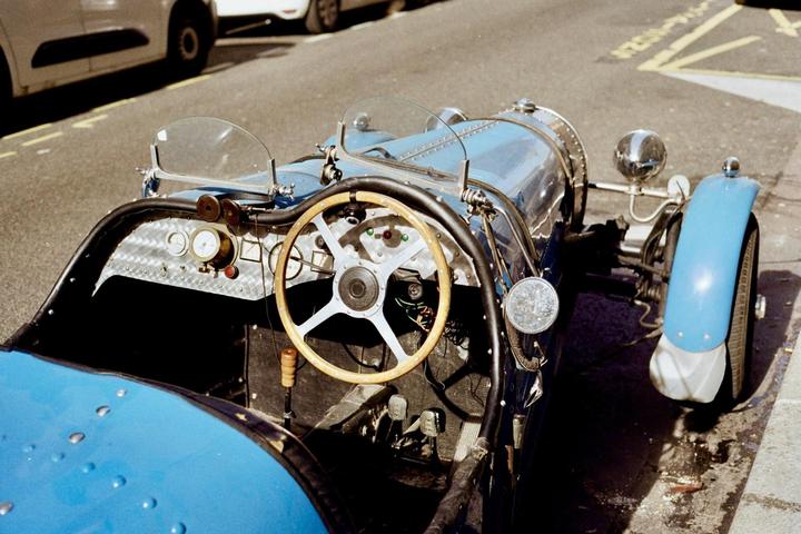 A blue vintage car with a wooden steering wheel is parked on a street.