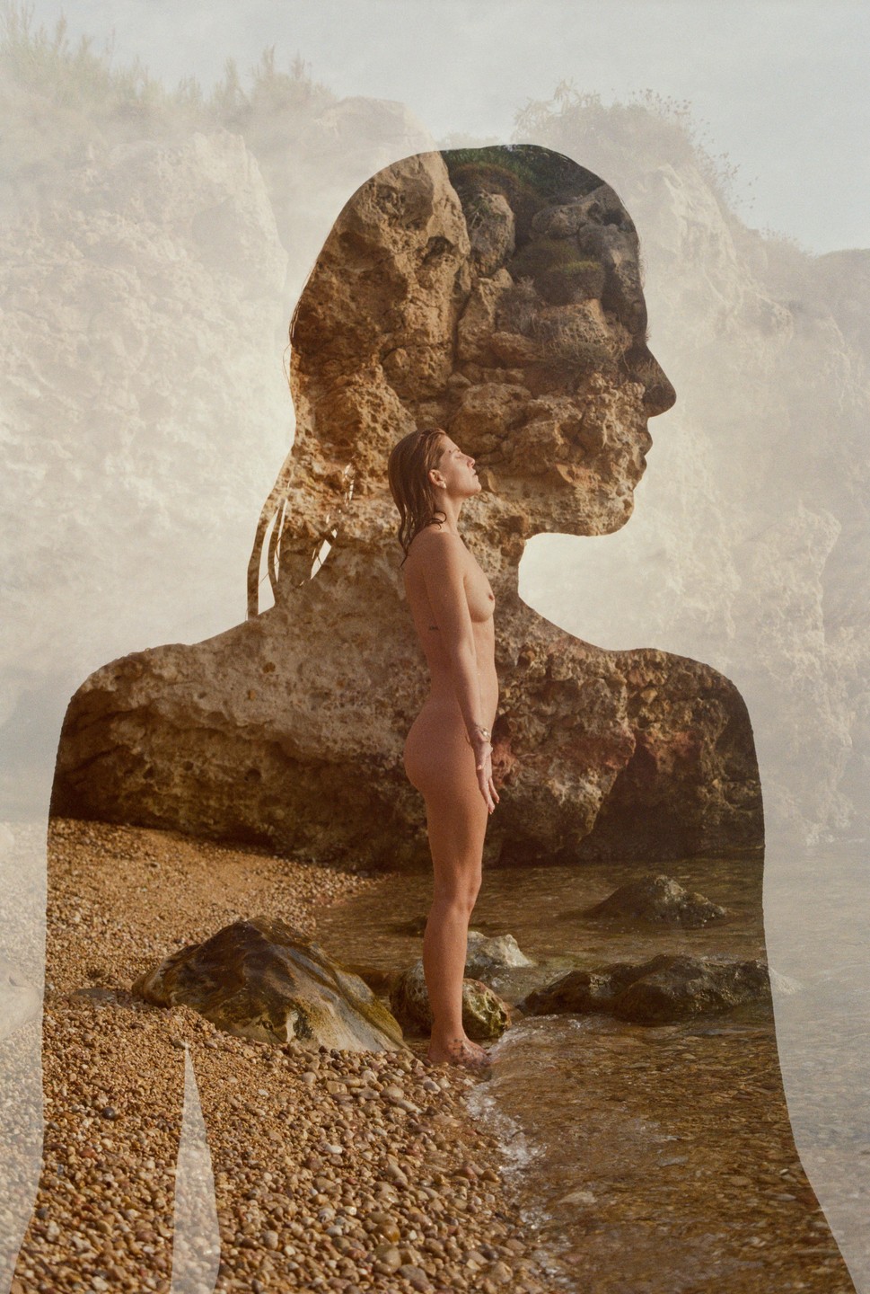 A double exposure shows a nude woman standing in shallow water on a rocky beach, superimposed over a rocky cliff face.