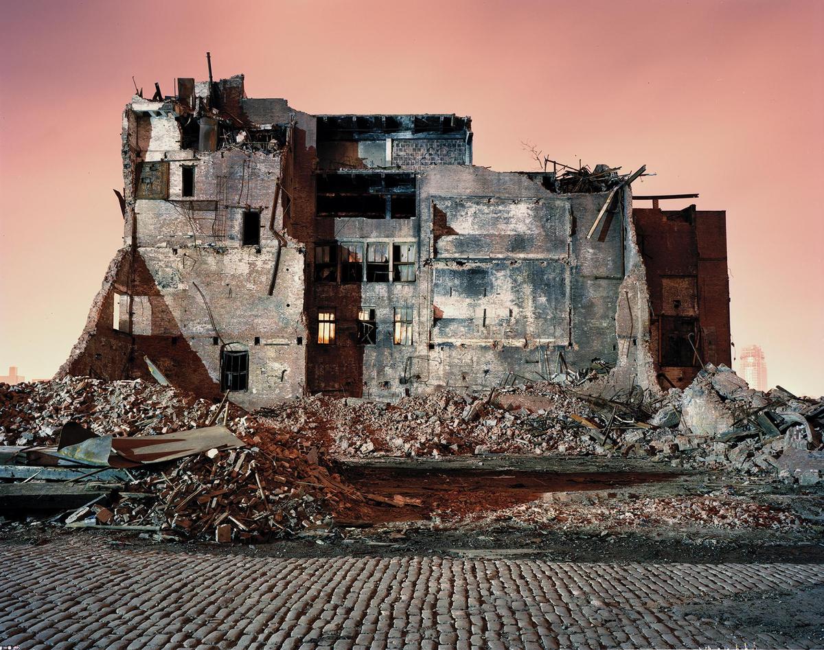 A large, partially demolished brick building stands over a pile of rubble with a cobblestone street in the foreground.