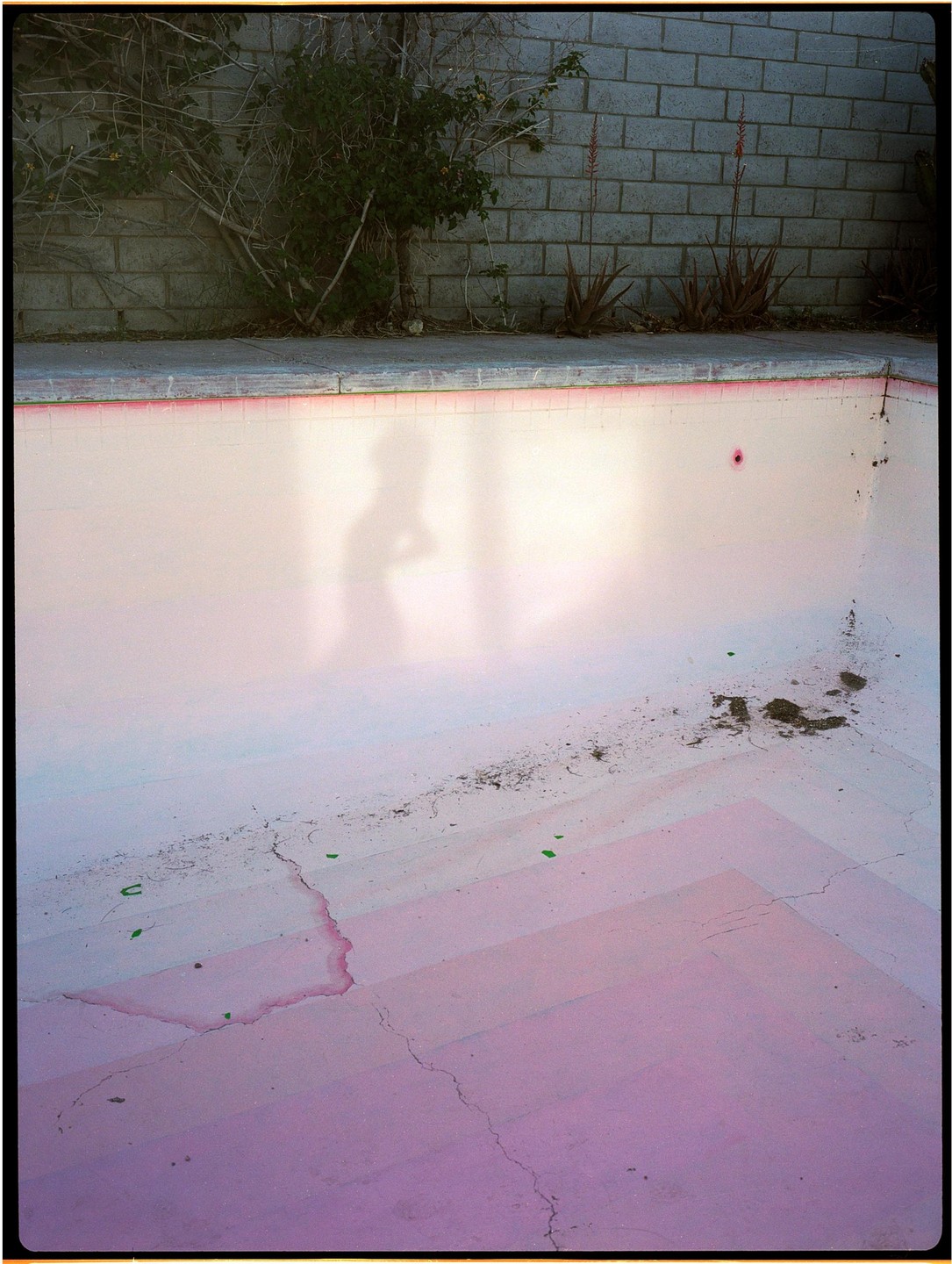 A shadow of a person is cast on the pink bottom of an empty swimming pool.