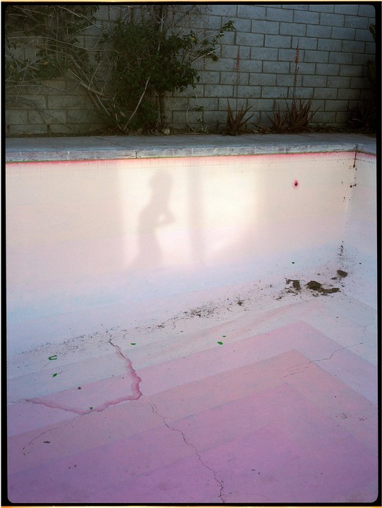A shadow of a person is cast on the pink bottom of an empty swimming pool.