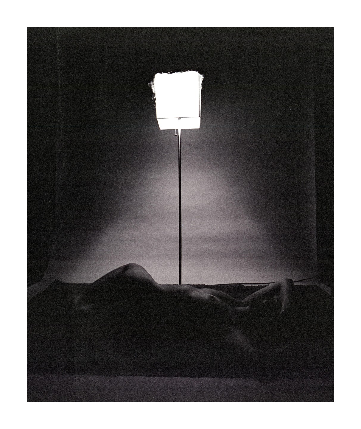 A nude woman lies on her side in a dark room, illuminated by a single bright light source.