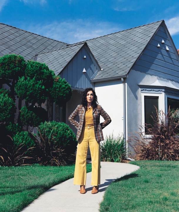 A woman stands on a curved sidewalk in front of a house with a blue roof.