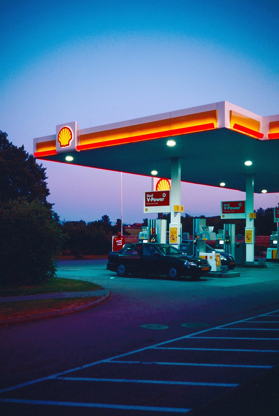 A black car is parked at a Shell gas station at dusk.