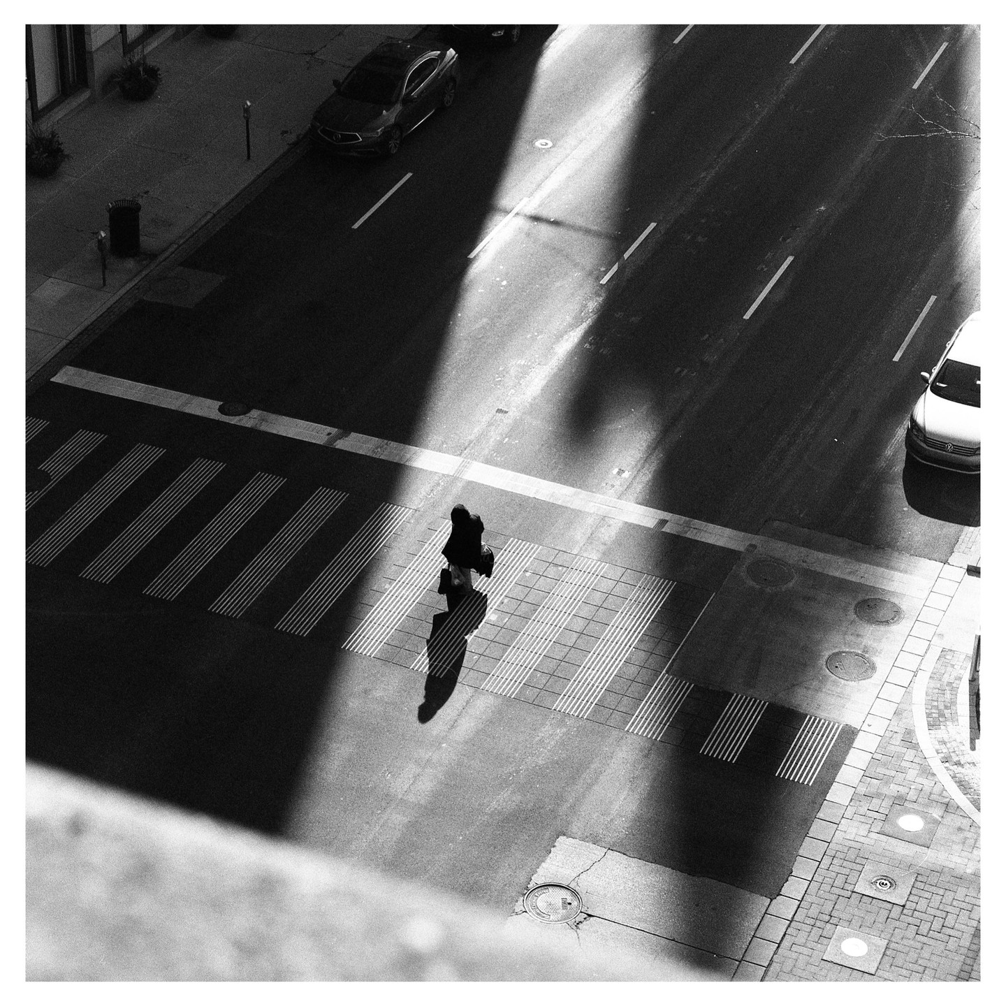 A person walks across a crosswalk on a city street, casting a long shadow.