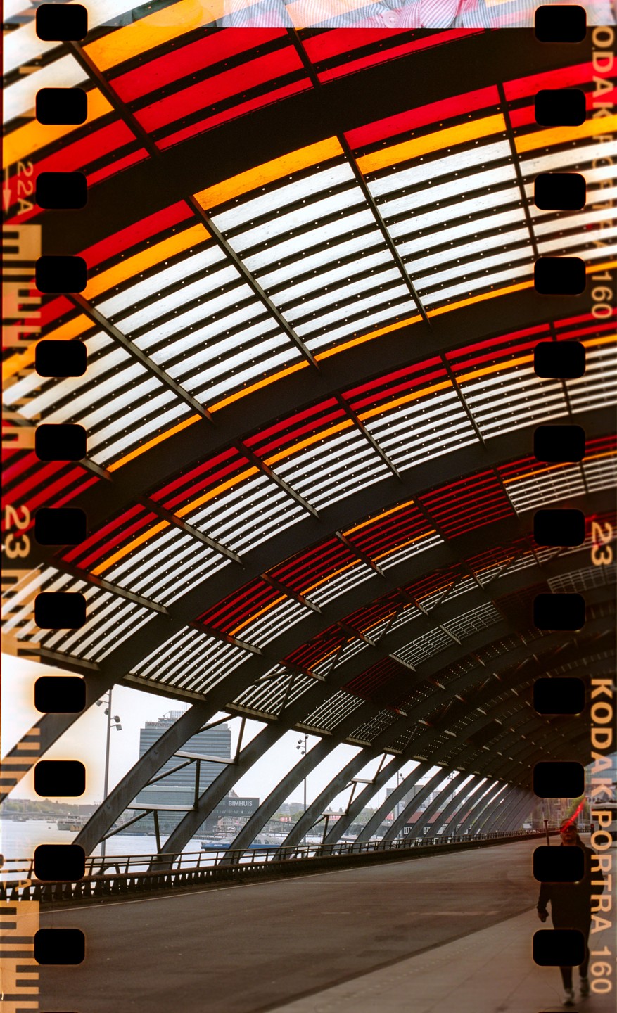 A person walks on a bridge with a colorful, striped arched roof overhead.