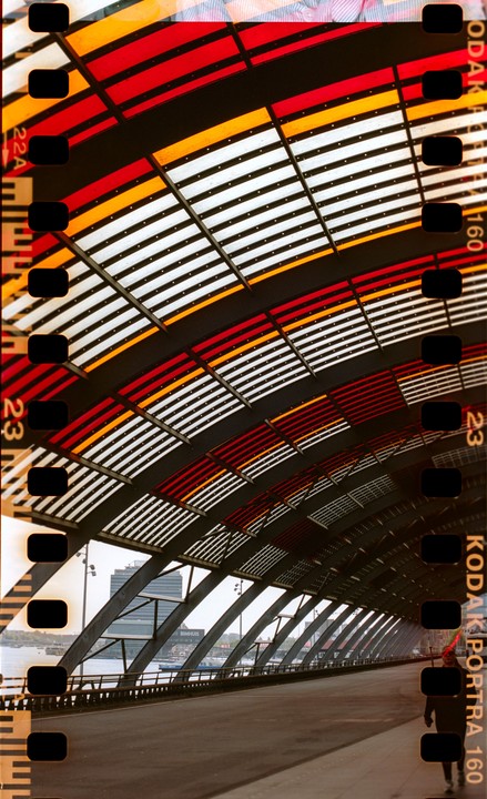 A person walks on a bridge with a colorful, striped arched roof overhead.