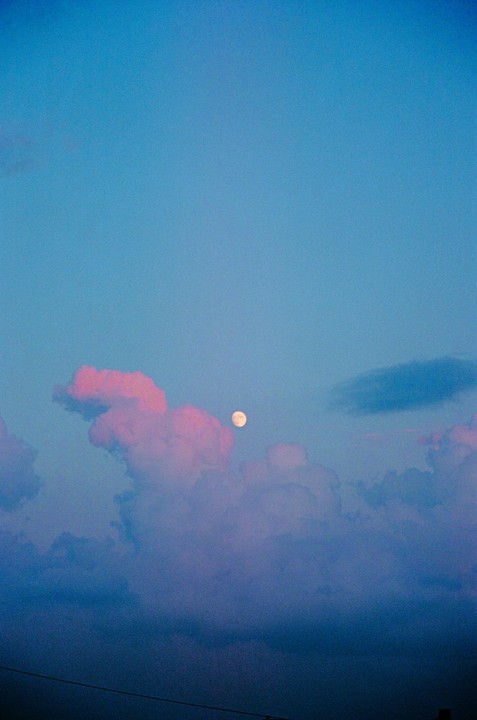 The moon is visible through pink and blue clouds in a blue sky.
