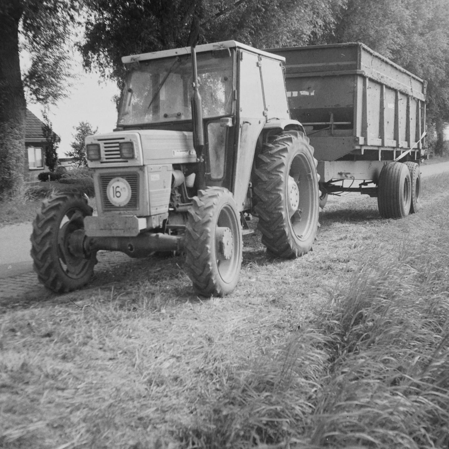 A tractor with a trailer is parked on a grassy path next to a road.