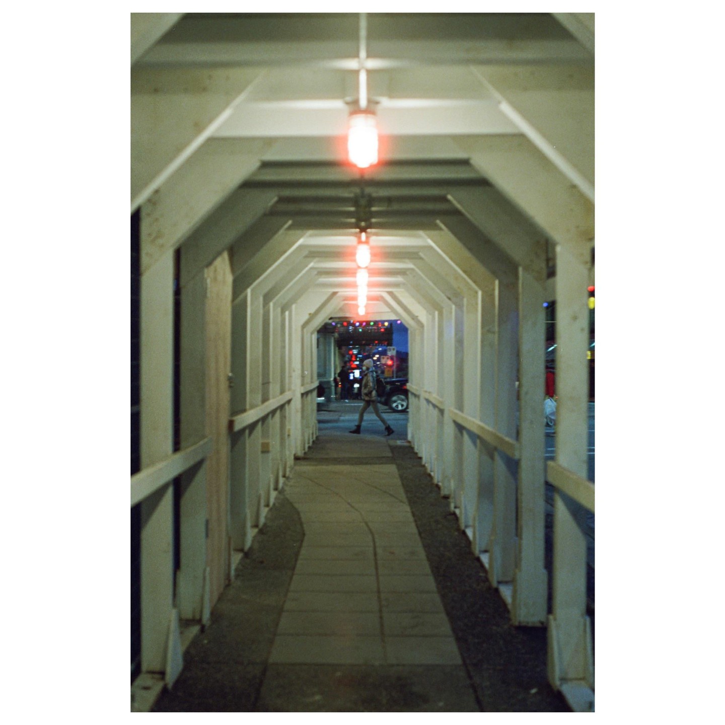 A person walks through a tunnel with red lights on the ceiling at night.