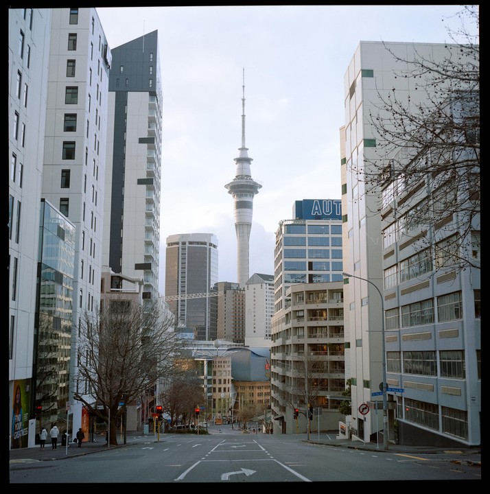 A wide street with tall buildings on either side leads to a distant tower in a city.
