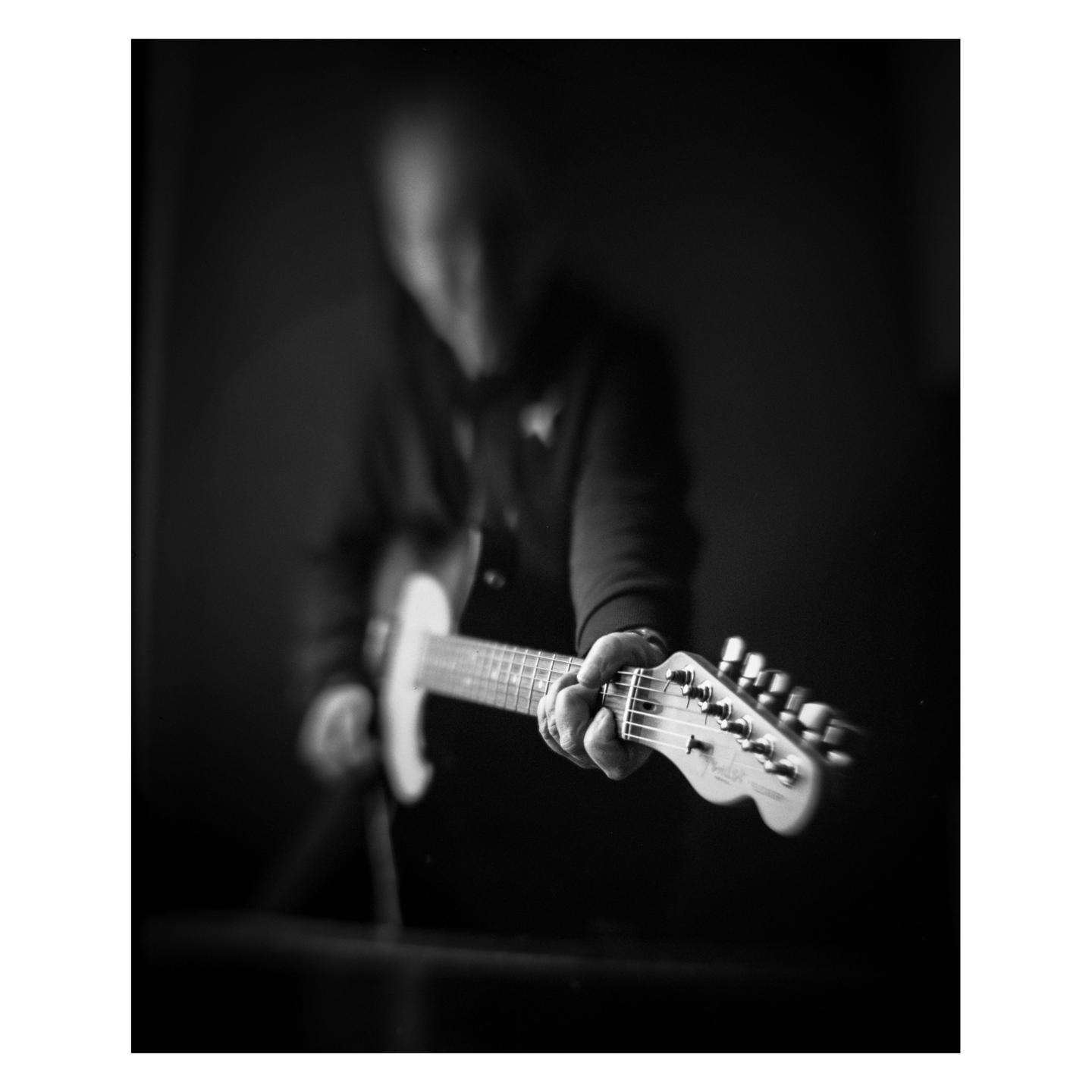 A man plays an electric guitar in a dark setting.