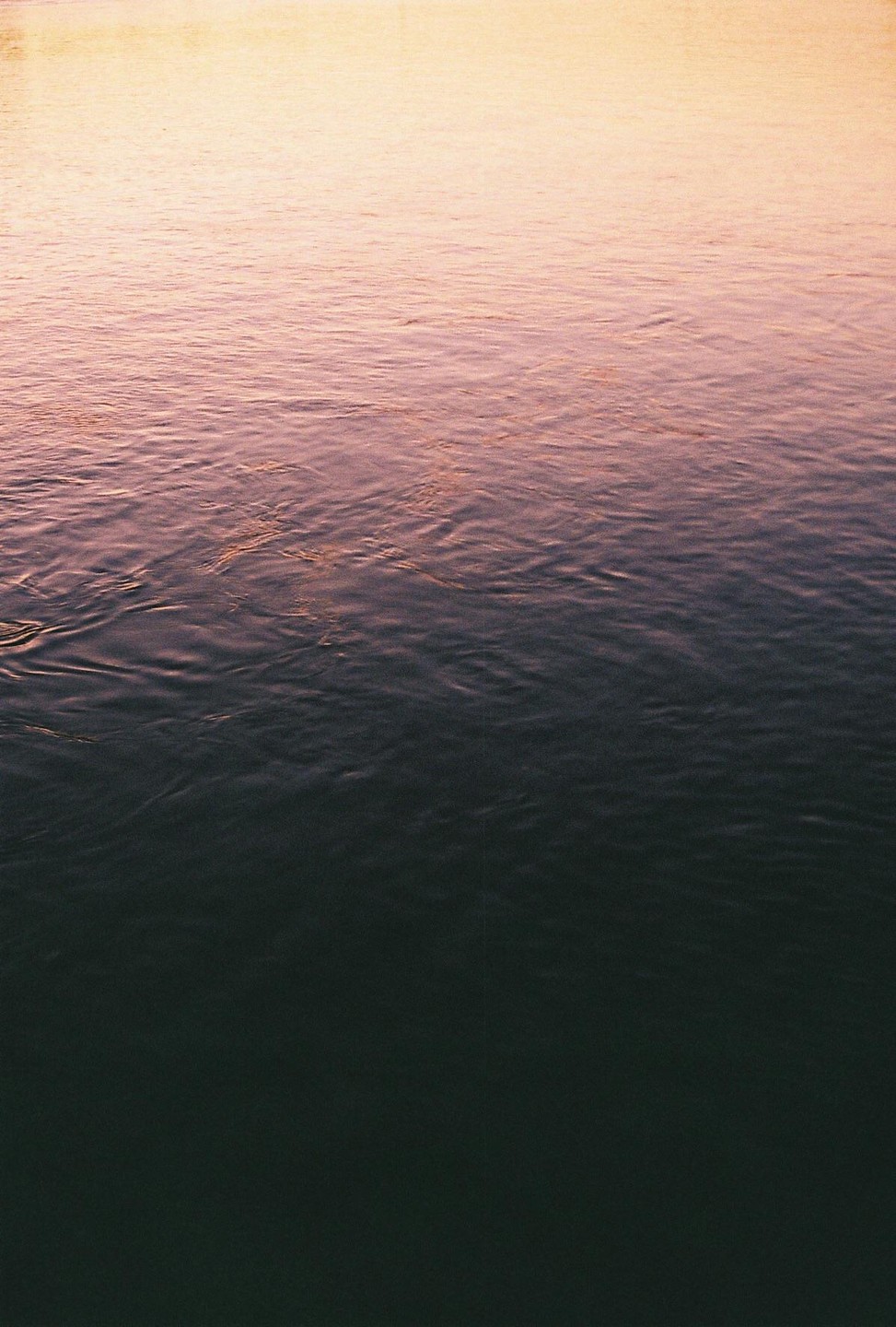 The surface of a body of water shows a gradient of color from light orange at the top to dark blue at the bottom.