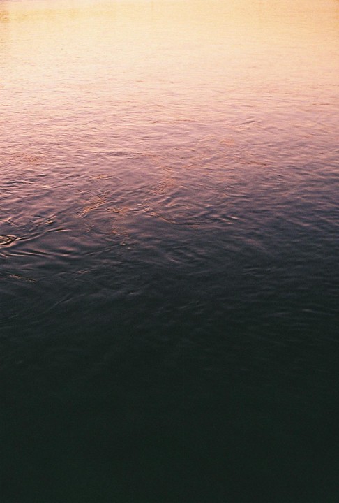 The surface of a body of water shows a gradient of color from light orange at the top to dark blue at the bottom.