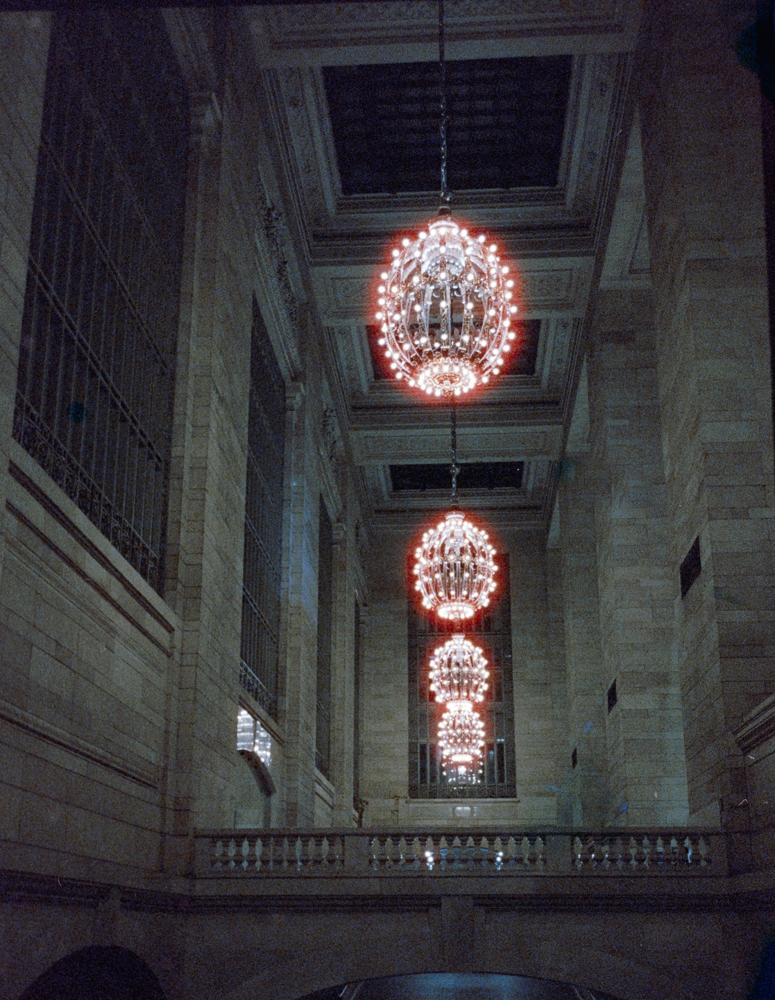 Three ornate chandeliers hang in a row from a high ceiling in a large hall.
