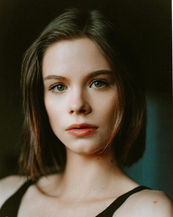 A woman with short hair and green eyes looks directly at the viewer.