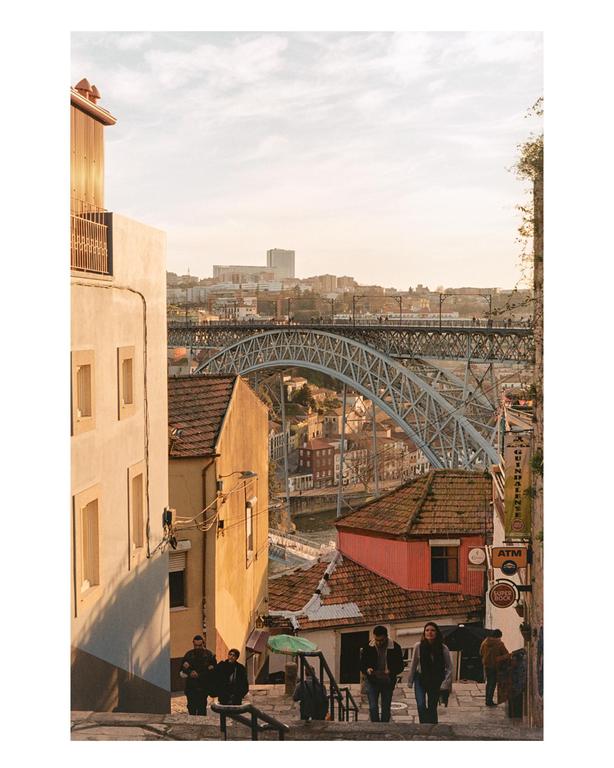 People walk down a street with buildings and a large metal bridge in the background.