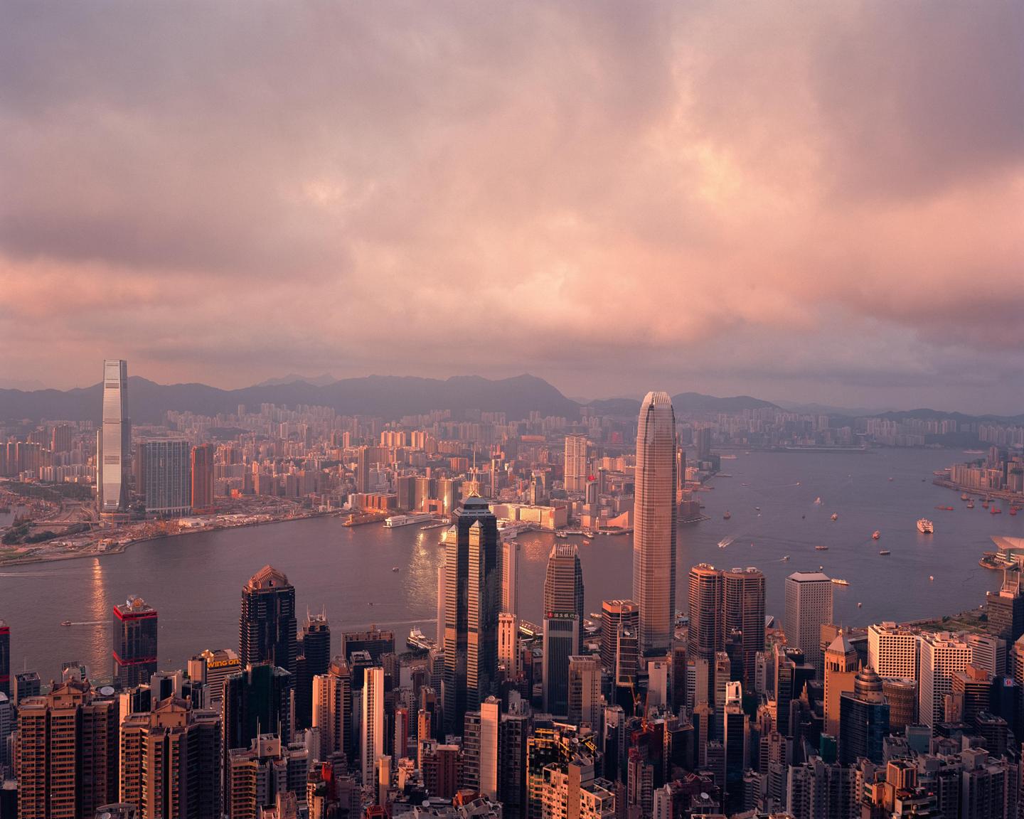 An aerial view of a city with many skyscrapers and a body of water with boats, under a cloudy sky.