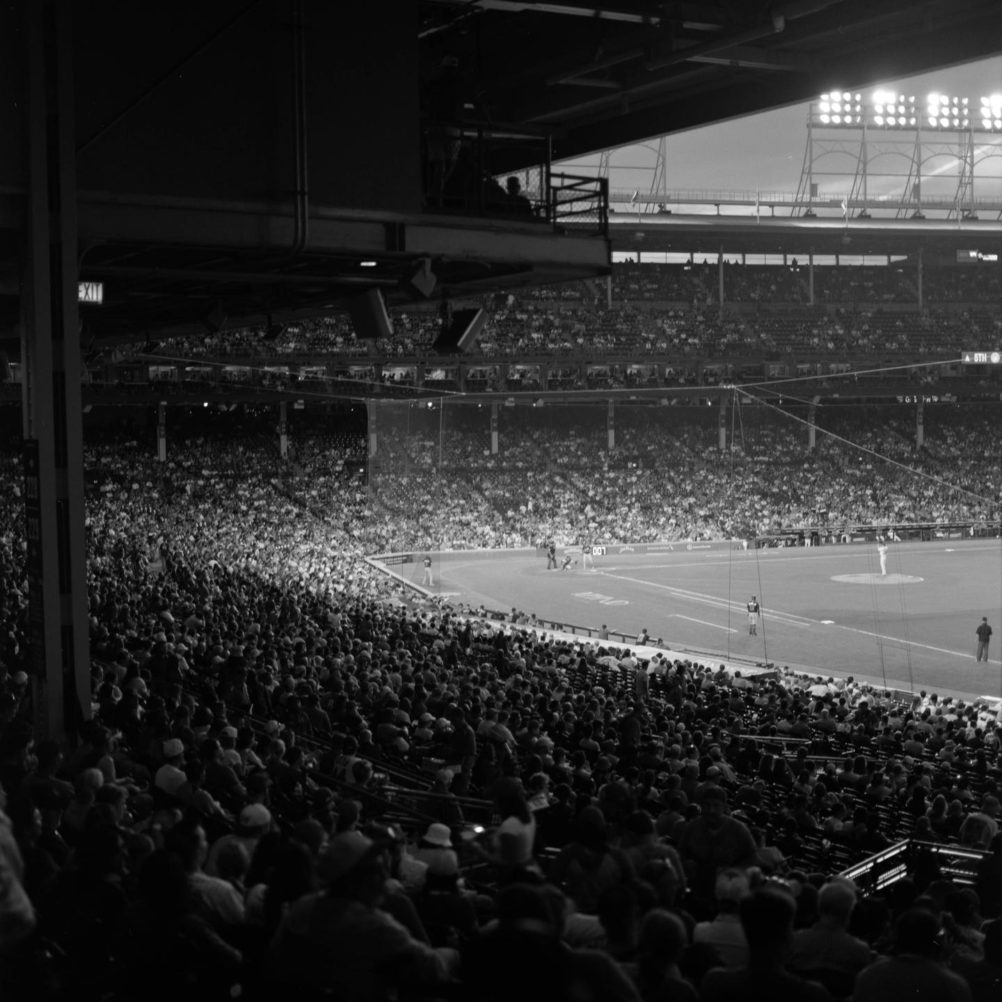 A large crowd watches a baseball game in a stadium at night.