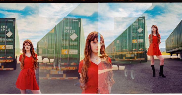A woman in a red dress is triple exposed in front of two green shipping containers.
