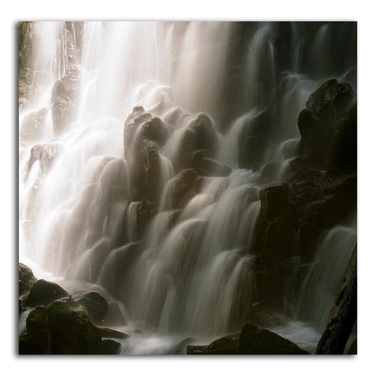 A waterfall cascades over dark rocks, creating a soft, misty effect.