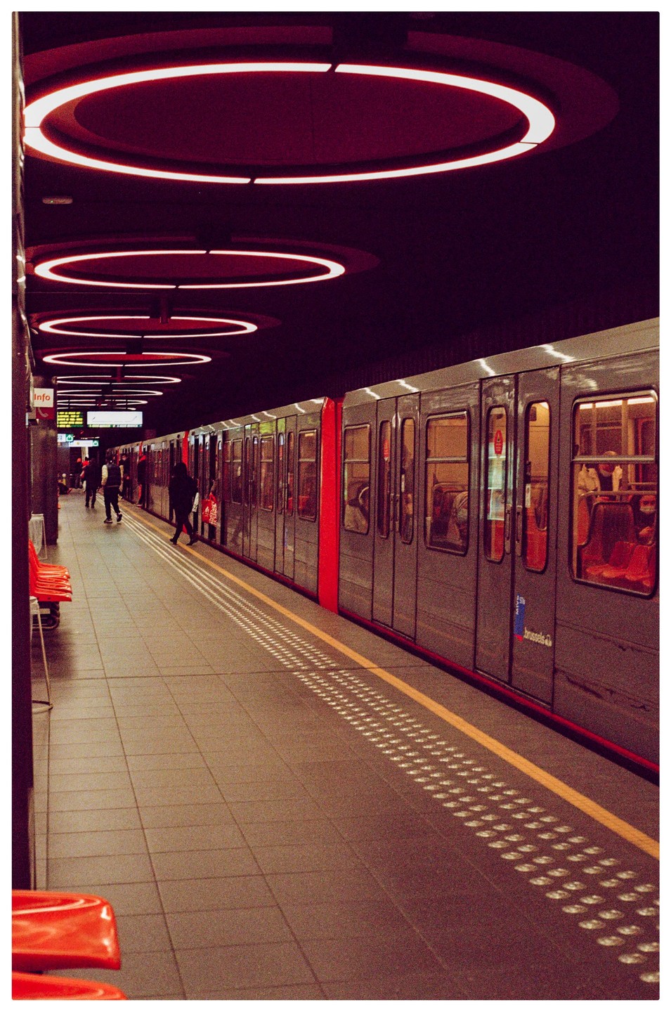 A subway train is stopped at a station platform with red circular lights on the ceiling.