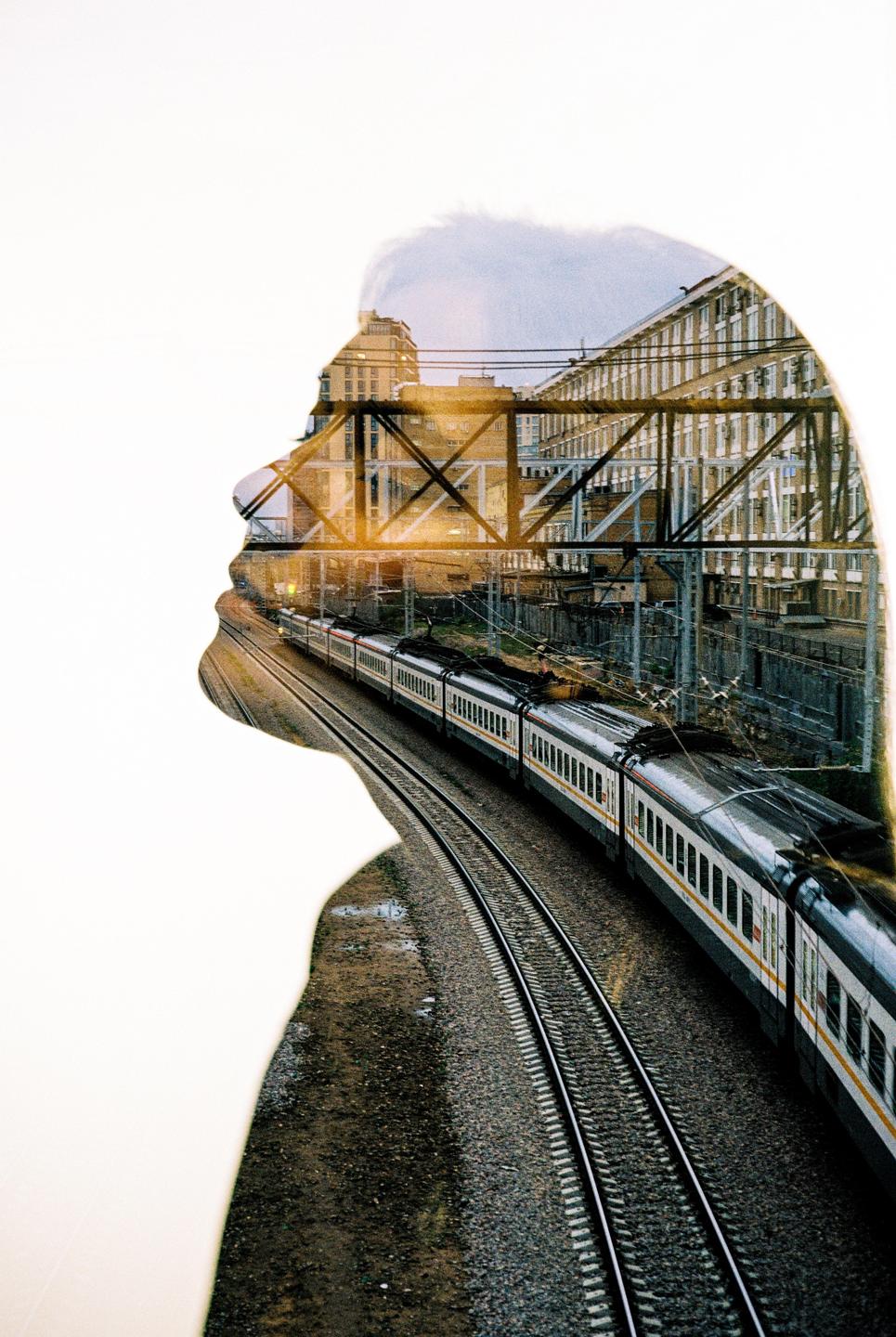 A double exposure shows the silhouette of a woman's head overlaid with a train on tracks next to buildings.
