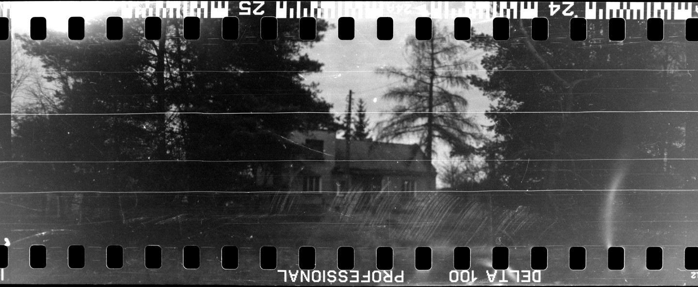 A house is visible through trees in a black and white image with film borders.