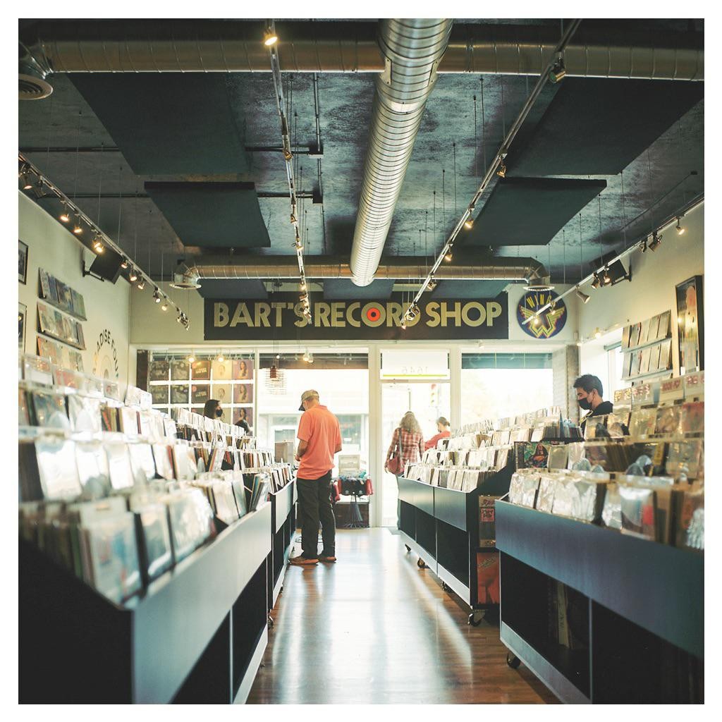 A man in an orange shirt looks at records in a record store.