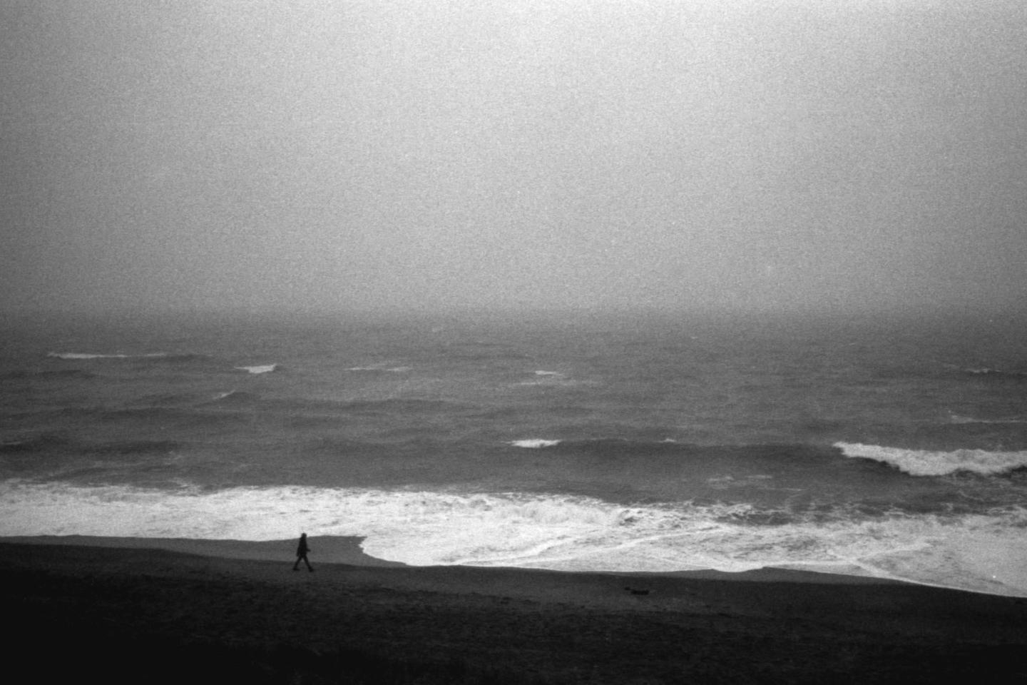 A person walks along a beach next to the ocean on a hazy day.