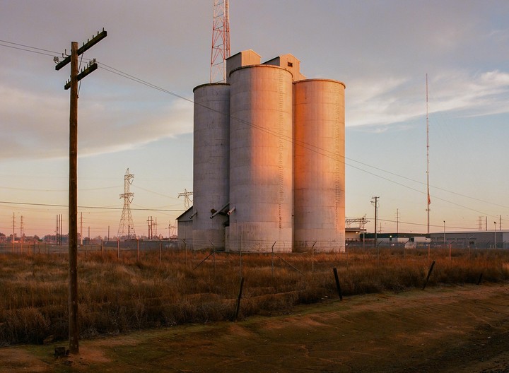 Three silos stand in a field with power lines and a utility pole in the foreground.