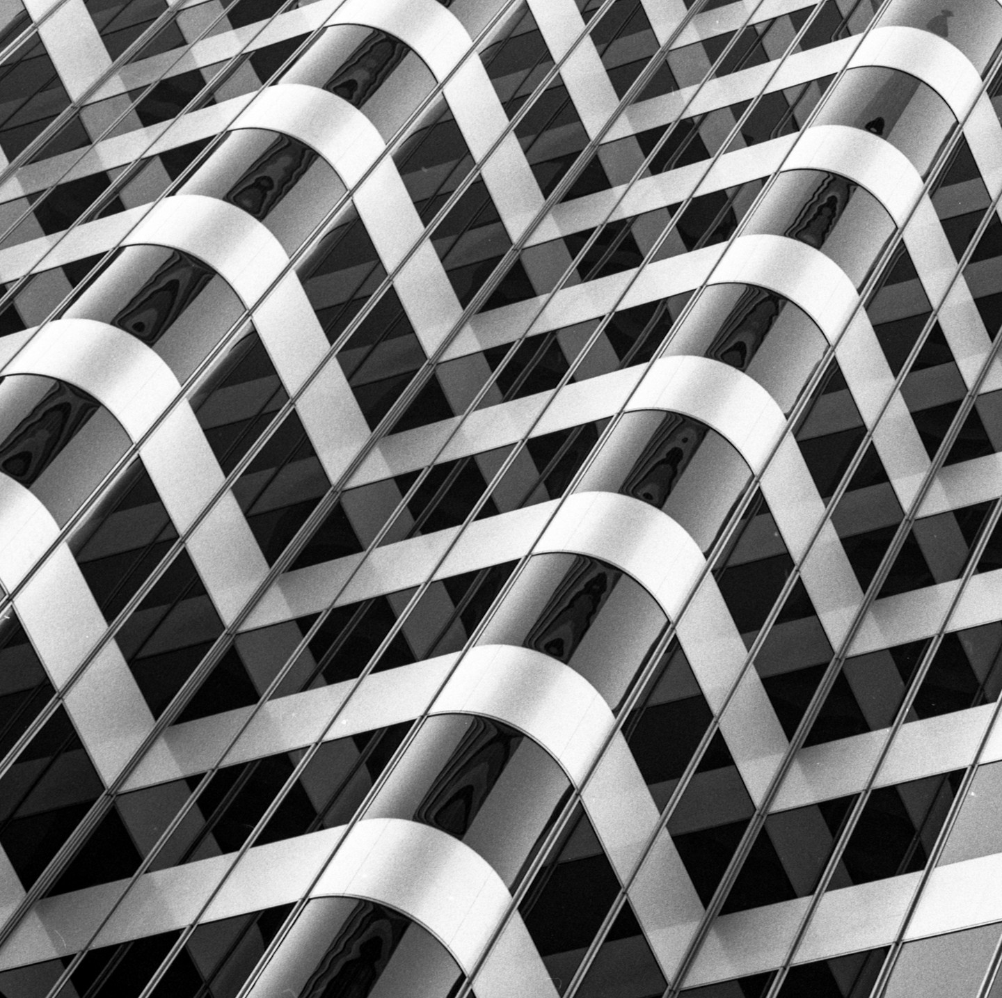 A black and white abstract image shows a building facade with a grid pattern of windows and curved reflective panels.