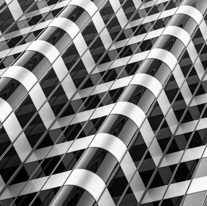 A black and white abstract image shows a building facade with a grid pattern of windows and curved reflective panels.