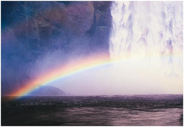 A rainbow stretches across a body of water with a powerful waterfall in the background.
