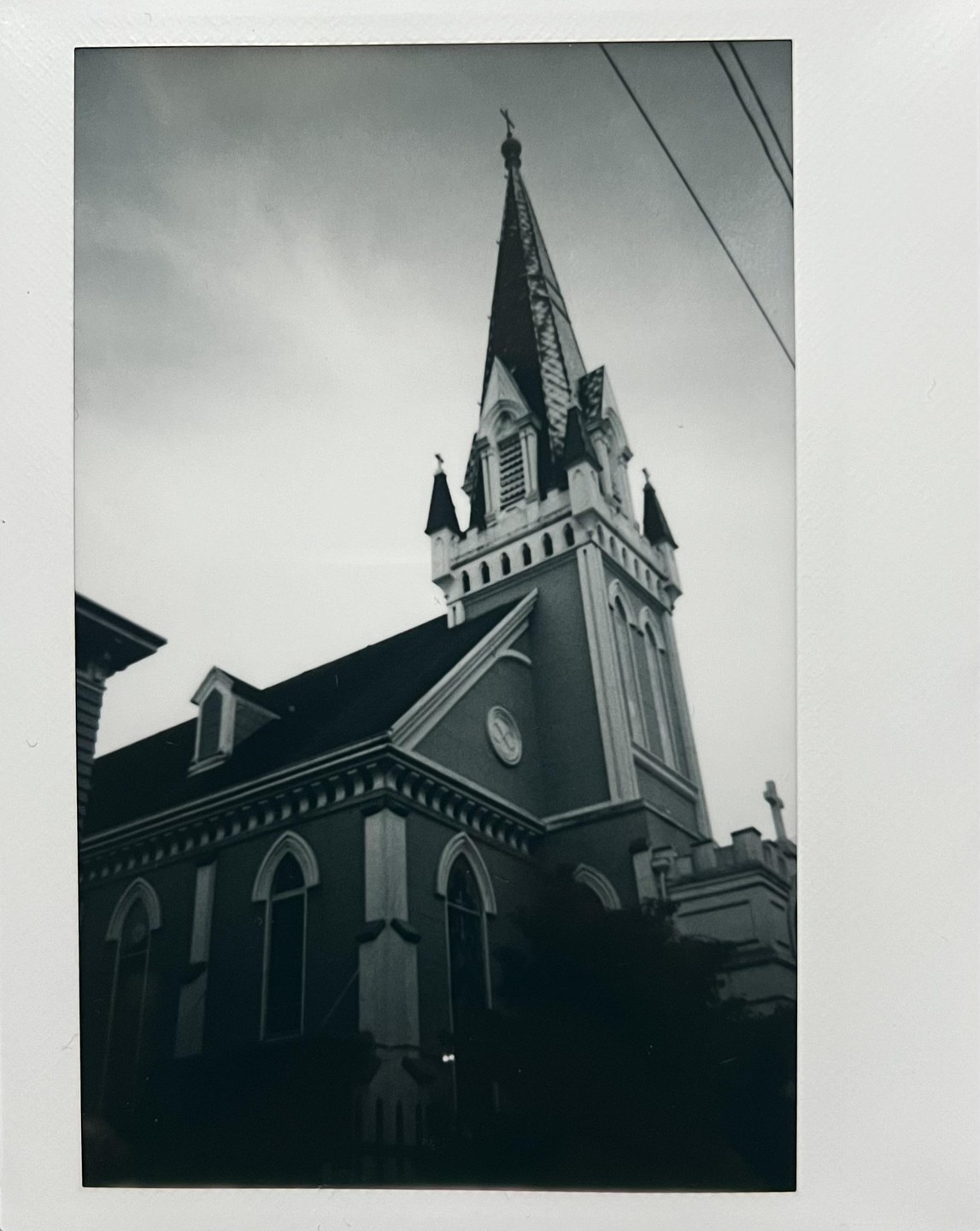 A tall church steeple with a cross on top rises into a cloudy sky.