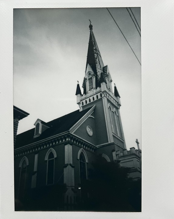 A tall church steeple with a cross on top rises into a cloudy sky.