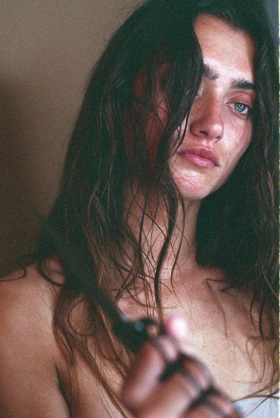 A woman with long, dark hair covering part of her face holds a dark object in her hand.