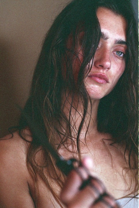 A woman with long, dark hair covering part of her face holds a dark object in her hand.