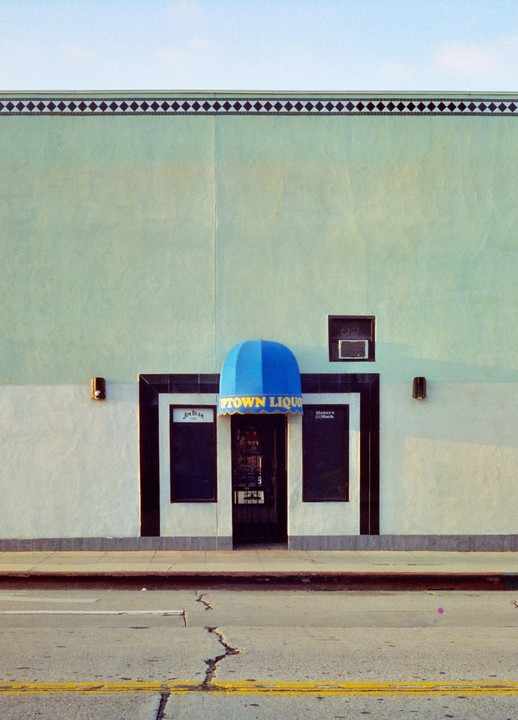A liquor store facade with a blue awning is seen from across the street.