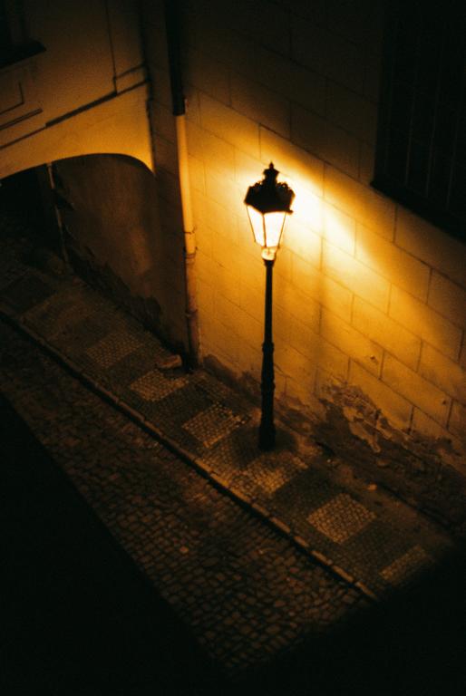 A single street lamp illuminates a cobblestone street and a stone wall at night.