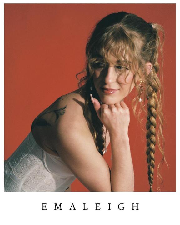 A woman with braided hair and a white top poses against a red background.