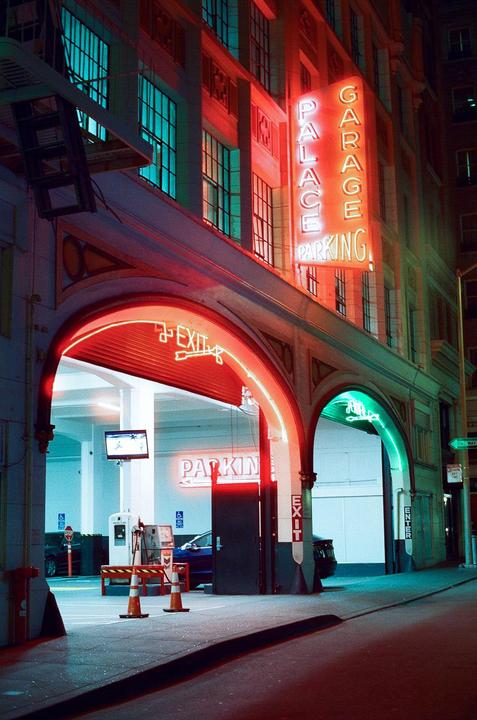 A neon sign for Palace Garage Parking illuminates the entrance to a parking garage at night.