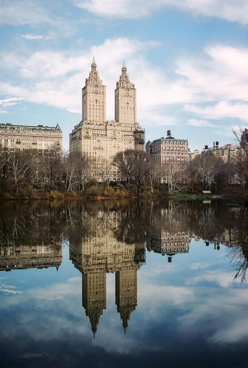 The San Remo building is reflected in the still water of a lake in Central Park.