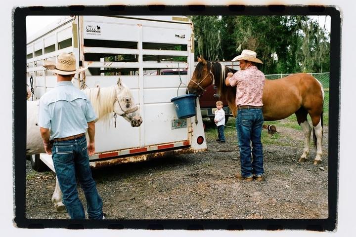 Two men and a child are with two horses next to a horse trailer.