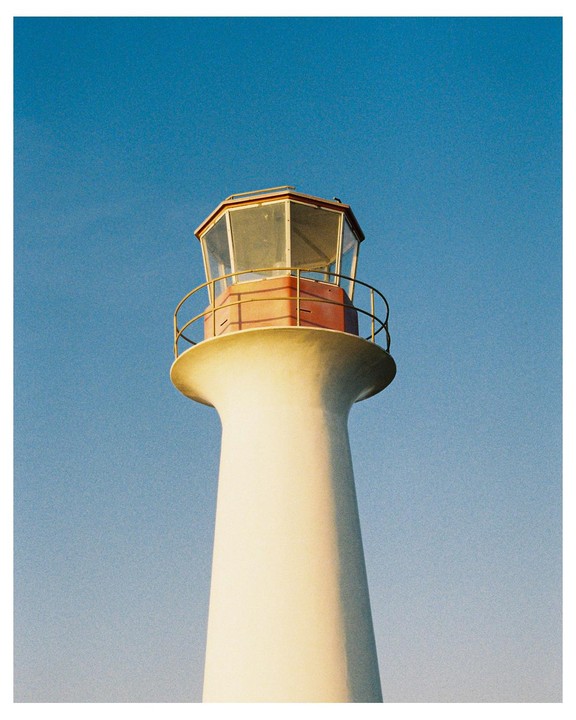 A white lighthouse with a red top stands against a clear blue sky.