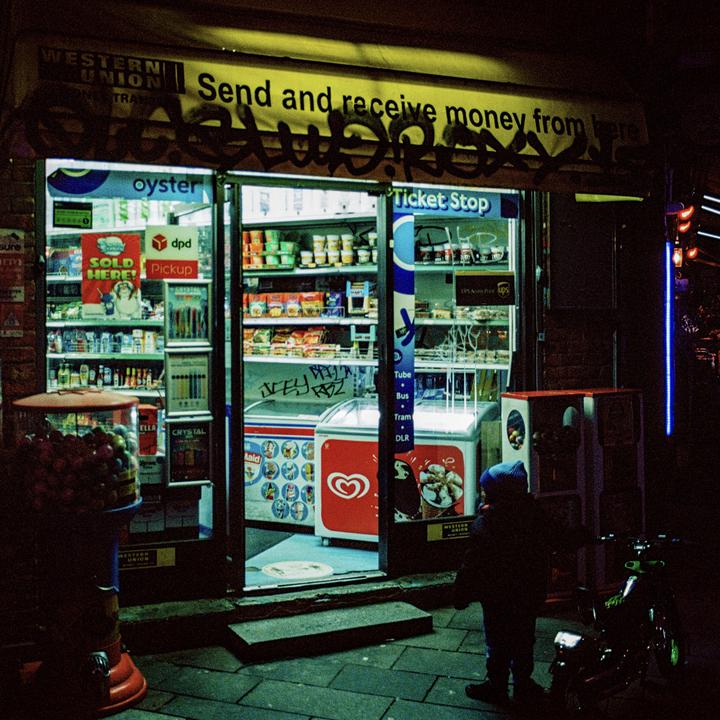 A child stands outside a brightly lit convenience store at night.
