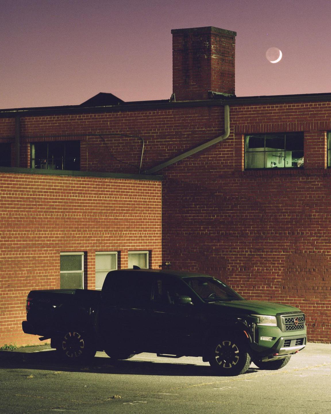 A dark pickup truck is parked in front of a brick building under a crescent moon.