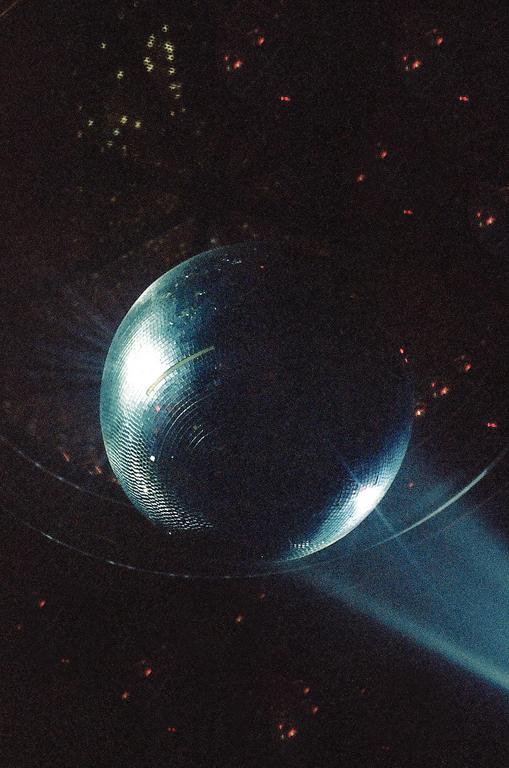 A disco ball reflects light in a dark room, casting small bright spots on the ceiling.
